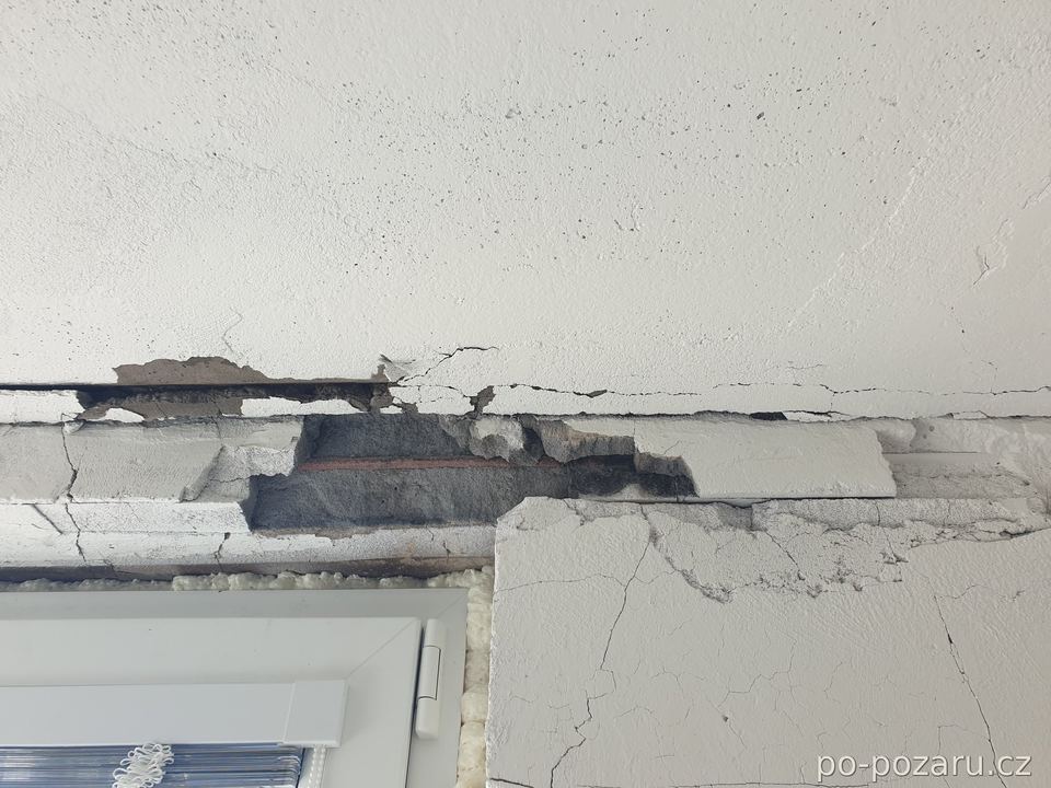 Detail trhlin a odprýsknutého betonu nad okenním otvorem po požáru.
