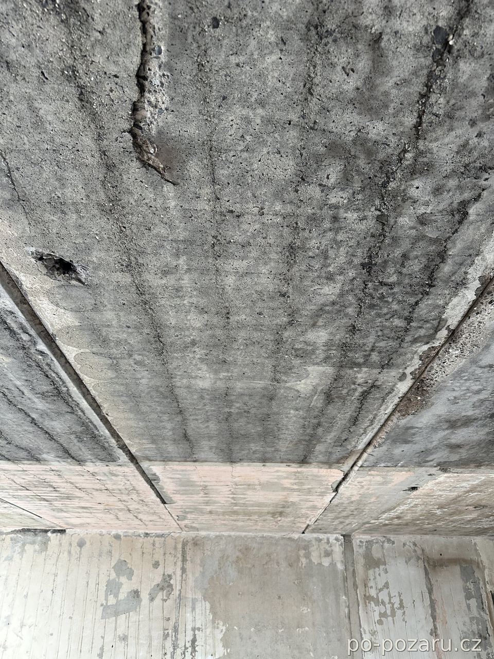 Detail stropních panelů se sazemi, trhlinami a tepelným poškozením betonu.